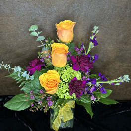 Orange roses and purple flowers in a glass vase with a yellow ribbon