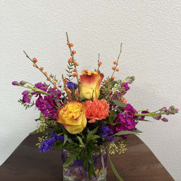 Mixed bouquet in a glass vase with yellow-orange roses and purple flowers