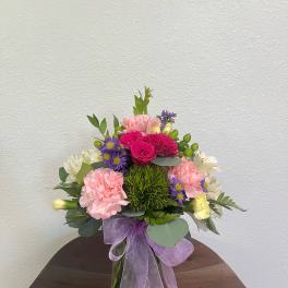 Mixed pink and purple bouquet in a glass vase with a lavender ribbon
