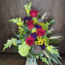 Tall mixed bouquet with red roses, yellow daisies, and purple blooms in a glass vase