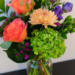 Mixed bouquet with coral roses, purple lisianthus, and a peach chrysanthemum in a glass vase