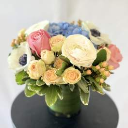Mixed bouquet of roses, ranunculus, and blue hydrangea in a green vase