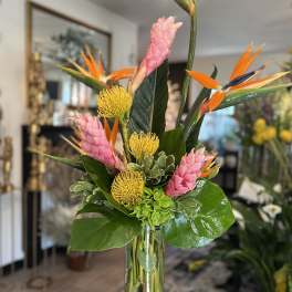 Tall tropical bouquet in a clear glass vase with pink and orange blooms