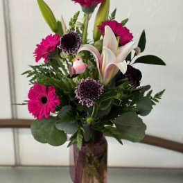Pink gerbera and lily arrangement in a tall vase with a small bird ornament