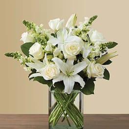 White lilies and roses arranged in a clear glass vase