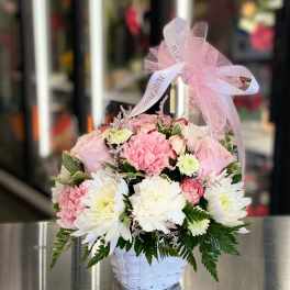 Pink and white flowers arranged in a white basket with a pink ribbon