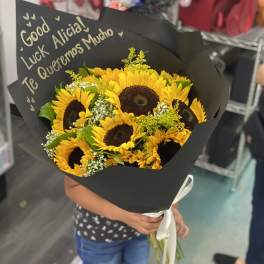 Bouquet of yellow sunflowers wrapped in black paper with a white ribbon