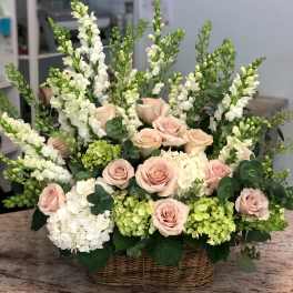 Basket arrangement of pale pink roses and white snapdragons with hydrangeas
