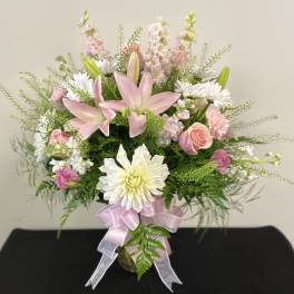 Pink lilies and white daisies in a glass vase with a pink ribbon