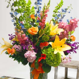 Tall mixed bouquet with lilies, roses, orchids, and blue flowers in a glass vase