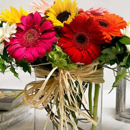 Bright gerbera daisies arranged in a clear square vase with raffia ribbon