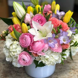 Mixed bouquet of pink, white, yellow, and lavender flowers in a white vase