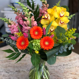 Mixed bouquet with yellow orchids, orange gerbera daisies, and pink snapdragons in a glass vase