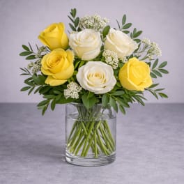 Yellow and white roses arranged in a clear glass vase