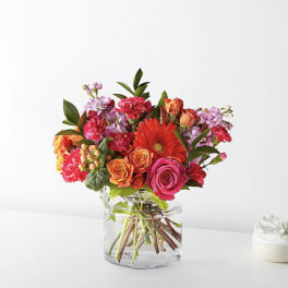 Mixed bouquet of roses, gerbera daisies, and carnations in a clear glass vase