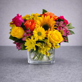 Colorful bouquet of roses, sunflowers, and daisies in a clear glass vase