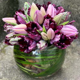 Pink and burgundy tulips clustered in a round glass vase lined with green leaves