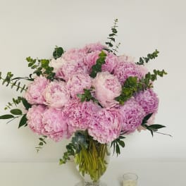 Large arrangement of pink peonies in a clear glass vase beside a small votive candle