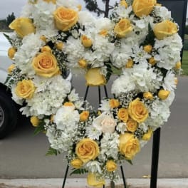 Heart-shaped floral wreath with yellow roses and white flowers on a stand