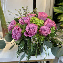 Pink roses arranged in a low vase with green hydrangea and foliage