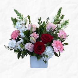 Mixed bouquet of red, pink, and white flowers in a square vase