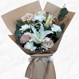 Bouquet of pale roses, white lilies, and chrysanthemums wrapped in tan paper