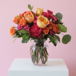 Bouquet of orange, yellow, and pink roses in a clear glass vase