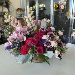 Mixed pink and purple flower arrangement in a woven basket