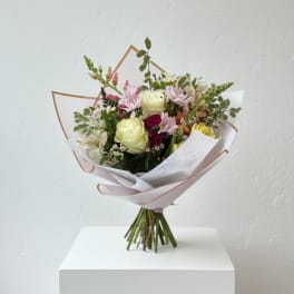 Hand-tied bouquet of pastel flowers wrapped in white paper
