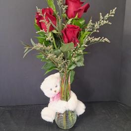 Red roses in a glass vase with a white teddy bear