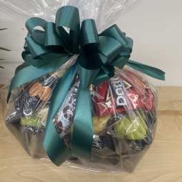 Gift basket with chocolates, candy, and cheese wrapped in clear cellophane with a large green bow