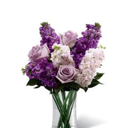 Purple and lavender flowers arranged in a clear glass vase