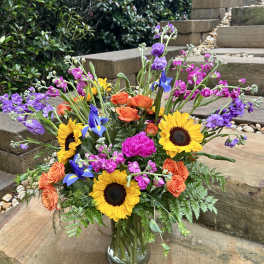 Colorful mixed bouquet in a clear glass vase with sunflowers, roses, and purple blooms