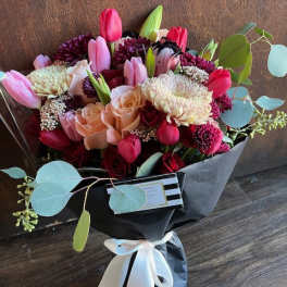 Bouquet of pink tulips, roses, and chrysanthemums wrapped in black paper