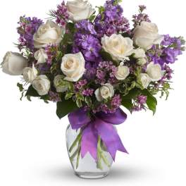 White roses and purple flowers in a glass vase with a purple ribbon