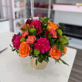Bouquet of orange roses, pink carnations, and green button mums in a glass vase