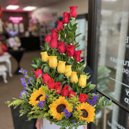 Tiered arrangement of red and yellow roses with sunflowers in a white box