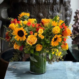 Bright mixed bouquet with sunflowers, roses, and orange blooms in a glass vase