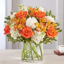 Orange roses and white flowers arranged in a clear glass vase