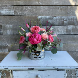 Pink floral arrangement in a silver vase on a white table