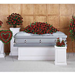 Funeral casket surrounded by red rose arrangements and a heart wreath