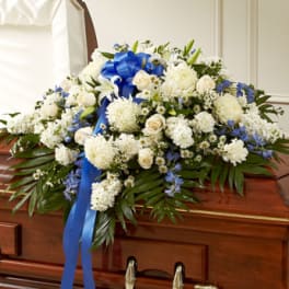 White floral casket spray with blue ribbon on a wooden casket
