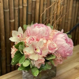 Pink floral arrangement in a square glass vase with roses and orchids