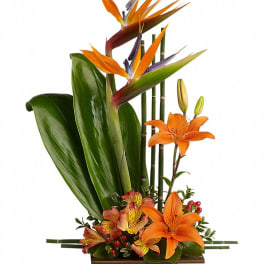 Tropical floral arrangement with orange lilies and bird-of-paradise in a rectangular vase