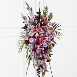 Tall standing spray of pink lilies and purple flowers with palm fronds on a metal easel