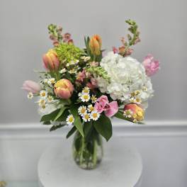 Mixed bouquet with tulips, white hydrangea, and small daisies in a glass vase
