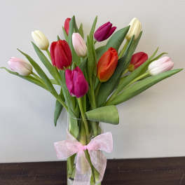 Bouquet of multicolored tulips in a clear glass vase with a pink ribbon