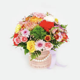 Colorful mixed flower bouquet in a wicker basket with a ribbon