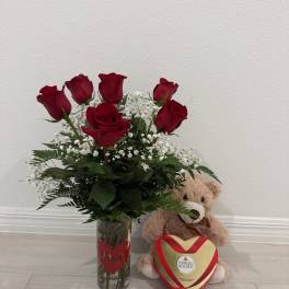 Red roses in a glass vase with a teddy bear and heart-shaped chocolate box