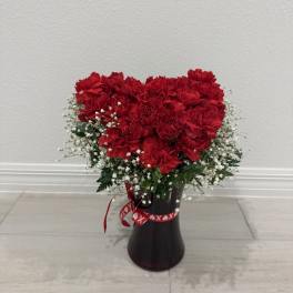Red carnations arranged in a dark vase with white baby's breath